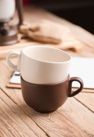 Two cups of coffee or tea stacked on old wooden table, with notebook, raffia sack, lampの写真素材