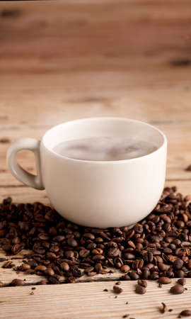 off white cup of coffee with smoke on rustic wooden table, with roasted coffee beansの写真素材