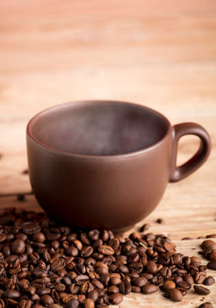 Brown cup of coffee with smoke on rustic wooden table, with roasted coffee beansの写真素材