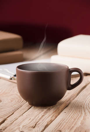 brown cup with chocolate, tea or coffee, hot steam, books on rustic wooden tableの写真素材