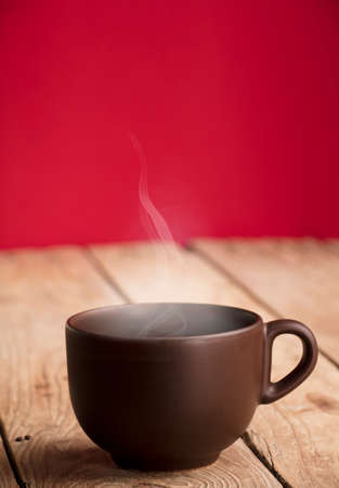 brown cup of hot drink with steam and smoke, on old table and red background.の写真素材