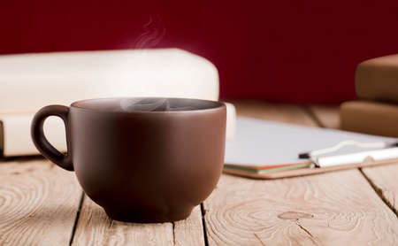 brown cup with chocolate, tea or coffee, hot steam, books on rustic wooden tableの写真素材