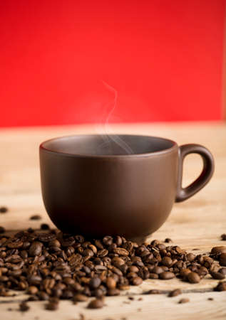 brown coffee cup with hot steam smoke and beans on wooden table, red backgroundの写真素材