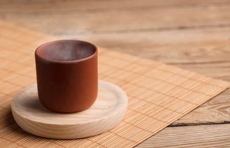 ceramic earthenware mug with steam on coasters, cane mat, rustic wooden table, brown backgroundの写真素材