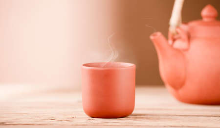 ceramic earthenware cup with hot steam and teapot on rustic wooden table, brown backgroundの写真素材