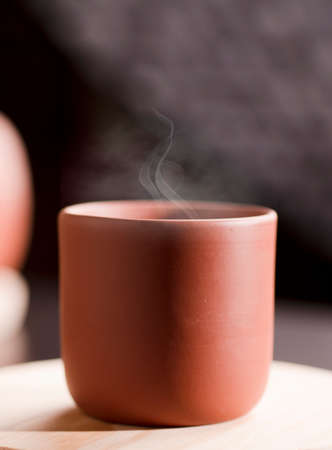 Earthenware mug with hot steam, with tea on white wood, dark background.の写真素材