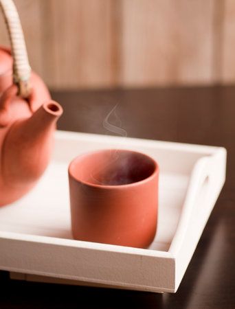 clay ceramic mug, hot with steam on white wooden tray and teapot or coffee pot with rustic wooden backgroundの写真素材