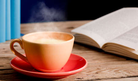 Yellow cup of tea with milk, hot steam, on wooden table, open book, blue background.の写真素材