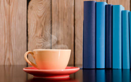 Yellow cup of coffee or tea with hot steam, on wooden table, with light blue and blue books. wood backgroundの写真素材