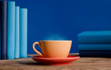 Yellow cup of coffee or tea with hot steam, on table wooden with light blue books and blue background.の写真素材