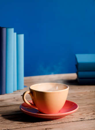 Yellow cup of coffee or tea with hot steam, on table wooden with light blue books and blue background.の写真素材