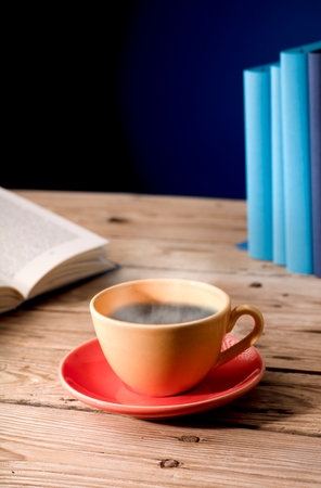 Yellow cup of tea with milk, hot steam, on wooden table, open book, blue background.の写真素材