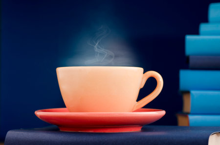 Yellow cup of coffee or tea with hot steam, on book with light blue books and blue background.の写真素材
