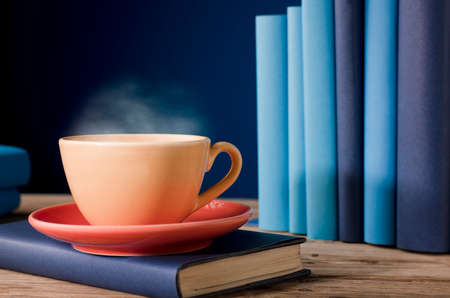 Yellow cup of coffee or tea with hot steam, on book with light blue books and blue background.の写真素材