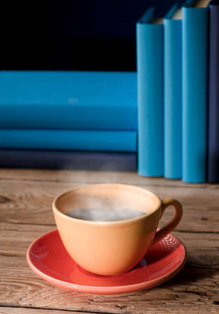 Yellow cup of coffee or tea with hot steam, on table wooden with light blue books and blue background.の写真素材