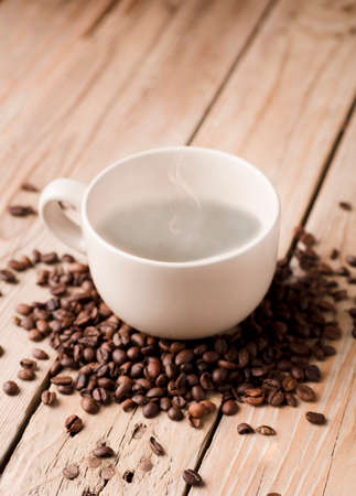 white cup of coffee with smoke on rustic wooden table, with roasted coffee beans.の写真素材