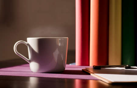 White ceramic mug with hot coffee on purple work desk and books with lgbt movement colorsの写真素材
