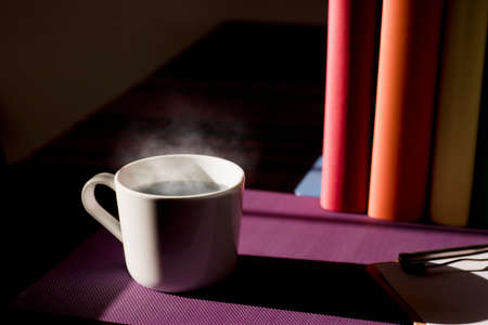 White ceramic mug with hot coffee on purple work desk and books with lgbt movement colorsの写真素材