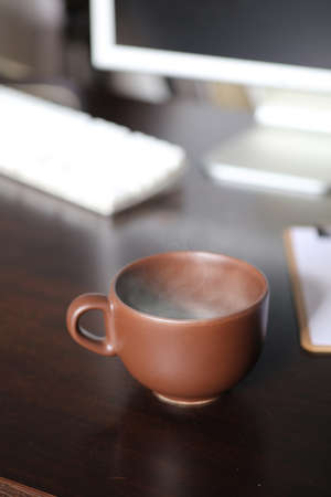 brown cup of coffee, with hot steam, on the work deskの写真素材