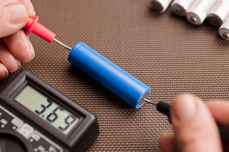 battery 18650 with volt calculator, voltmeter in the hands of a man, red positive pole, black negative pole, on a work tableの写真素材