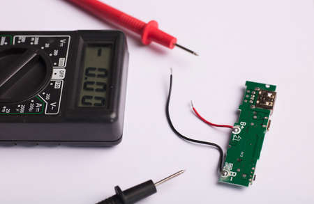 Electronic charging circuit with multimeter with red and black poles, checking voltage and amps, white backgroundの写真素材