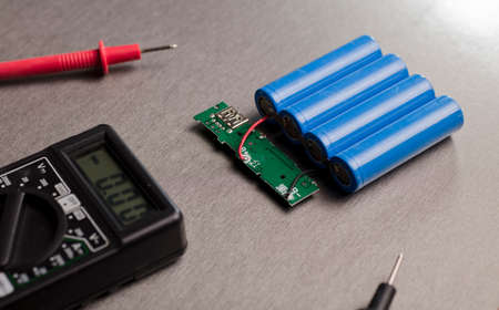 Charge indicator circuit, multimeter red and black poles 18650 blue batteries, gray background....