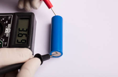 18650 blue battery, multimeter red and black poles in the hands of man checking voltage and amps...