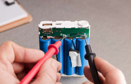 Charge indicator circuit, multimeter red and black poles in the hands of man checking voltage and amps, 18650 blue batteries, gray background. power bankの写真素材