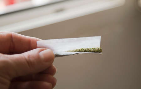 marijuana cigarette in man hands, home room backgroundの写真素材