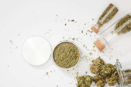 top view of marijuana buds with grinder accessories, glass bottles, and white backgroundの写真素材
