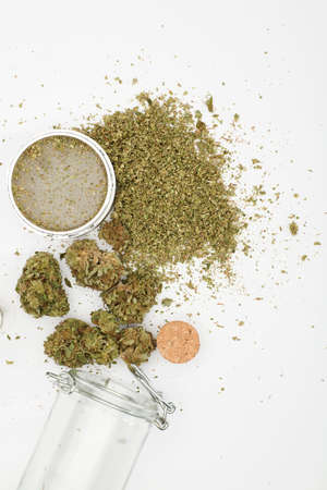 top view of marijuana buds with grinder accessories, glass bottles, and white backgroundの写真素材