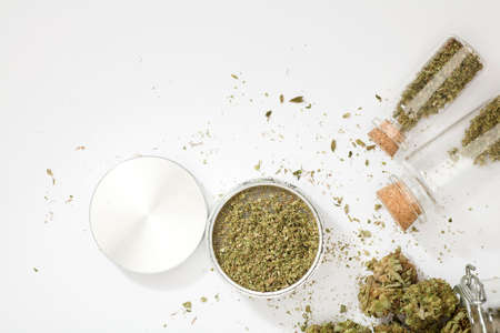 top view of marijuana buds with grinder accessories, glass bottles, and white backgroundの写真素材
