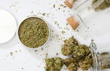 top view of marijuana buds with grinder accessories, glass bottles, and white backgroundの写真素材