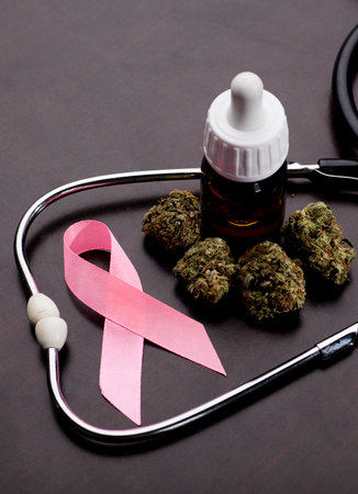 cancer pink ribbon with medical marijuana buds, stethoscope, oil bottle, brown background.の写真素材