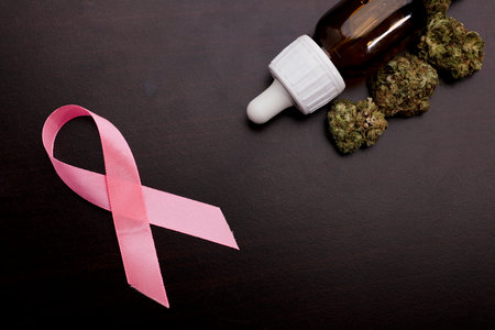 cancer awareness pink ribbon with marijuana buds and drop dispenser bottle, dark wood background.の写真素材