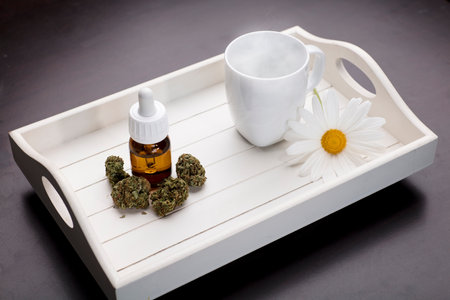 marijuana bud oil drop dispenser and white cup,daisy flower,on white tray dark wood backgroundの写真素材
