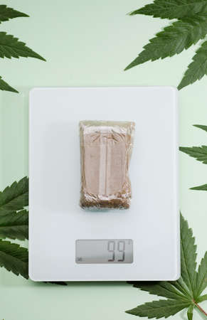 packaged hashish tablet on weight scale, marijuana leaves, green backgroundの写真素材