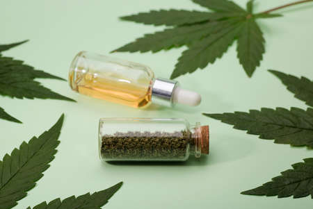 ground marijuana bite in glass jar. marijuana oil in drops dispenser bottle and green leaves, green backgroundの写真素材