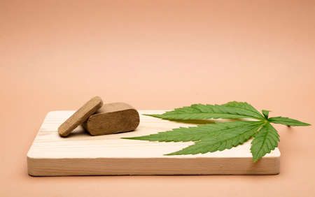 hashish tablet, hashish portion 100 grams, with large marijuana leaf, on wood, brown background