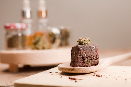 Chocolate cupcake muffins with cannabis buds in wooden spoon, oil pot and cooking jars. Marijuana hemp in food dessert. Chocolate herb muffins cooking. Marijuana cake on a brown wooden table.の写真素材