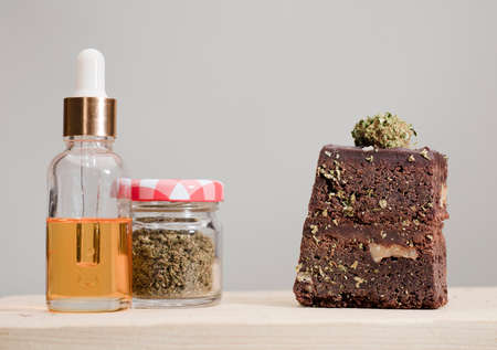 dropper bottle glass marijuana oil drops and chocolate cupcake muffins with cannabis buds. Marijuana hemp in food dessert. Chocolate herb muffins cooking. Marijuana cake on a brown wooden table.の写真素材