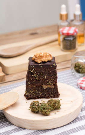Chocolate cupcake muffins with cannabis buds in wooden spoon, oil pot and cooking jars. Marijuana hemp in food dessert. Chocolate herb muffins cooking. Marijuana cake on a brown wooden table.の写真素材