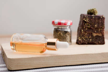 dropper bottle glass marijuana oil drops and chocolate cupcake muffins with cannabis buds. Marijuana hemp in food dessert. Chocolate herb muffins cooking. Marijuana cake on a brown wooden tableの写真素材