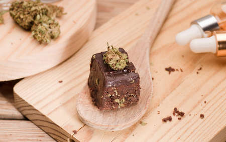 Chocolate cupcake muffins with cannabis buds in wooden spoon, oil pot and cooking jars. Marijuana hemp in food dessert. Chocolate herb muffins cooking. Marijuana cake on a brown wooden table.の写真素材