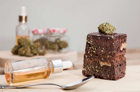 dropper bottle glass marijuana oil drops and chocolate cupcake muffins with cannabis buds. Marijuana hemp in food dessert. Chocolate herb muffins cooking. Marijuana cake on a brown wooden tableの写真素材