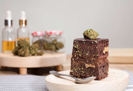 Chocolate cupcake muffins with cannabis buds in wooden spoon, oil pot and cooking jars. Marijuana hemp in food dessert. Chocolate herb muffins cooking. Marijuana cake on a brown wooden table.の写真素材