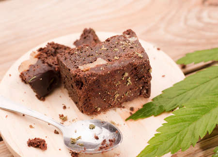 piece of brownie with marijuana, on wooden board with spoon and green cannabis leafの写真素材