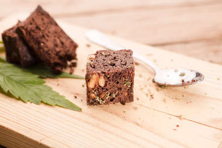piece of brownie with marijuana, on wooden board with spoon and green cannabis leafの写真素材