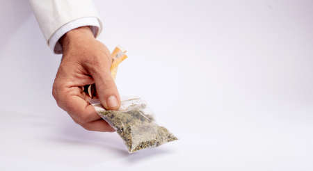 Naturopathic dispensary employee hands over a bag of medical marijuana and takes the collection money with the other hand, on a white counterの写真素材
