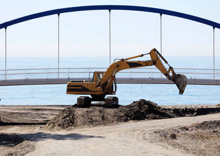excavation and earthmoving machinery, bulldozer with bridge and sea in the background. Cleaning the...